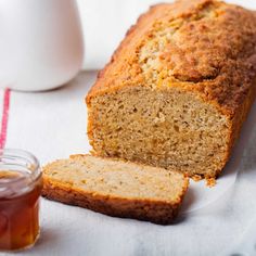 a loaf of banana bread next to a jar of honey on a white tablecloth