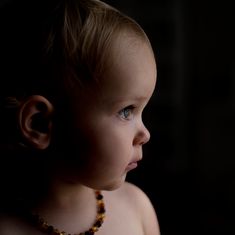 a young child wearing a beaded necklace looking off into the distance with dark background