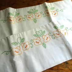 two white napkins with orange and green flowers on them sitting on a wooden table