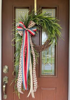 a wreath hanging on the front door of a house with red, white and blue ribbons