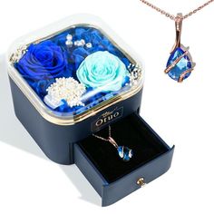 an open jewelry box with blue roses and pearls in it, next to a necklace