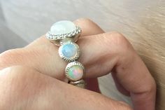 "A gorgeous shimmery round Cabochon Moonstone statement ring accented with a halo of white topaz complemented with 7 cabochon opals on the shank, handcrafted in sterling silver, makes this a unique engagement ring or great statement ring.(r-c-183) These are cabochon opals on the shank, which extreme care needs to be taken not to break the stones as they rank 6 on Mohs hardness scale meaning, they are a soft and fragile gemstones. Avoid immersing in water or washing the dishes with the ring on an Elegant Moonstone Ring With Gemstone Accents, White Opal Ring With Accent Stones, White Moonstone Ring With Round Band, Unique White Multi-stone Moonstone Ring, Unique Jewelry With Halo Detail, Bohemian Wedding Rings With Gemstone Accents, White Round Multi-stone Jewelry, Adjustable White Round Cut Crystal Ring, Opal Rings With Gemstone Accents