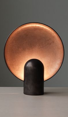 a table lamp sitting on top of a white counter next to a black vase with an orange light in it