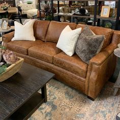 a brown leather couch sitting in a living room next to a coffee table and bookshelf