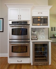 two ovens and a refrigerator in a kitchen with hardwood floors, white cabinets and wood flooring