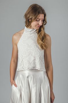 "The 'Aster' halter neck top This halter neck top is handmade in off-white cotton lace, lined in a soft organic cotton jersey. The neck tie is in organic cotton/ silk satin, which has a gentle sheen to it. The ties can be be tied at the back of the neck with a bow or left long. The top closes at the back with little covered buttons and rouleaux loops. This top is individually made to order in sizes XXS - XXL, please refer to size chart below. It can also be made to custom sizes/lengths. For sizing advice or to submit your measurements please get in touch.  It is available to order in off-white/ ivory. The standard length is 18\" from shoulder to hem. Made from 95% cotton, 5% nylon. Lined in 100% organic cotton jersey.  This top is made to order, designed, cut and stitched by me in England. Fitted Halter Neck Top For Wedding, Fitted Lace Halter Neck Top, Fitted Halter Neck Lace Top, White Delicate Lace Cropped Top, Spring Wedding Halter Neck Top, Chic Cropped Tops For Wedding, White Fitted Feminine Halter Top, Spring Wedding Fitted Halter Top, Delicate Lace Crop Top