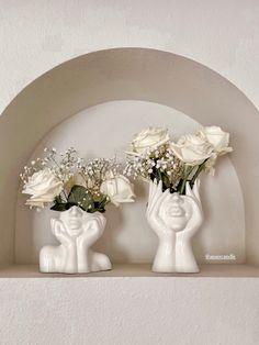 two white vases with flowers in them on a shelf