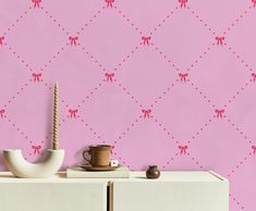 a pink wall with red bows on it and a white cabinet in the foreground