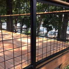 a wooden deck with black iron fencing around it and some trees in the back ground