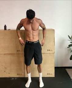 a man with no shirt standing in front of a wooden box and wearing white socks