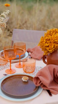 the table is set with plates, glasses and flowers in vases on top of it