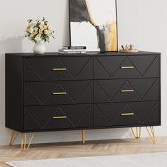 a black dresser with gold legs and a painting on the wall in front of it