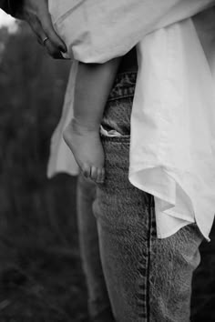 a black and white photo of a person holding a child's hand in their pocket