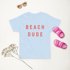 Our most popular design but with new colors!  Minimalistic Beach Babe and Beach Dude T-shirts for your toddlers! The perfect t-shirt to complete your toddlers summer outfit!  This summer T-shirt for Toddlers is perfect for your beach vacation. Works perfectly for cute instagram pictures or your family album and your toddler will love it! Perfect for sibling matching or matching with friends! Our new Beach Dude color is a fun coral and our new Beach Babe color is blue turquoise.  The t-shirts are Playful Cotton T-shirt For Vacation, Playful T-shirt For Summer Adventures, Playful Letter Print T-shirt For Vacation, Fun Beach Season Family Vacation T-shirt, Playful Crew Neck T-shirt For Beach, Playful Letter Print Top For Beach, Playful Short Sleeve Tops For Beach Season, Playful Letter Print Beach Top, Fun Cotton T-shirt For Summer Activities