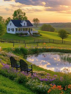 a white house sitting on top of a lush green hillside next to a pond and flowers