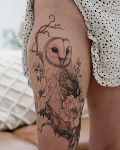 an owl tattoo on the leg of a woman's thigh, with flowers around it