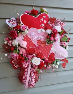 a heart shaped wreath hanging on the side of a house with valentine's day decorations