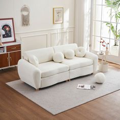 a white couch sitting on top of a wooden floor next to a rug and window