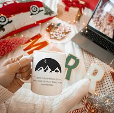 a person holding a coffee mug in front of a laptop computer on a bed with christmas decorations