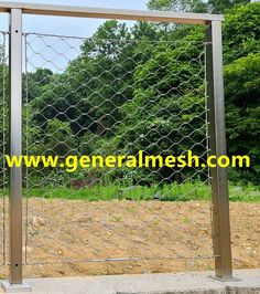 a large metal fence is in the middle of a dirt field with trees and bushes behind it