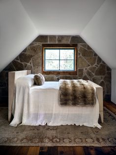 a bedroom with stone walls and a white bed in the corner, along with an area rug on the floor