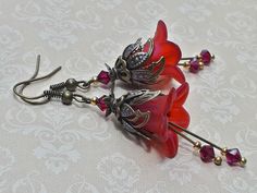 RUBY RED FLOWER EARRINGS ▪️▪️▪️▪️▪️▪️▪️️▪️▪️▪️▪️▪️▪️ These delicate antique style red flower earrings earrings are made with hand painted Lucite fairy flowers in iridescent red. They have matching coloured Siam red Swarovski crystals for beautiful sparkle when they move. Ornate floral bead caps compliment the flowers and antique bronze ear wires finish them. A perfect summer accessory or gift for nature and garden lovers. 💜MATERIALS *Lucite Flowers  *Antique Bronze Findings *Swarovski Crystals Red Bohemian Flower Earrings, Bohemian Red Flower Earrings, Red Bohemian Dangle Flower Earrings, Red Bohemian Drop Flower Earrings, Whimsical Red Drop Earrings, Red Dangle Earrings With Flower Charm, Red Bohemian Jewelry With Flower Charm, Whimsical Red Jewelry With Matching Earrings, Red Whimsical Nickel-free Earrings