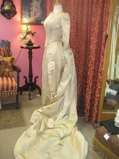 "1880's, 34\" bust, ecru silk faille, bustled and trained skirted wedding gown. A 19th century take on an 18th century lace up, low cut bodice. Bodice has a sharply pointed bottom, below waist, and 3/4 length cuffed sleeves. The bodice curves over hips, and is shorter in back than front. Bustled skirt has steel covered hoops built into back of skirt , and elaborate drapery forming into a long long train. Skirt has scalloped edge at bottom of the front, the bottom of train has a covered dust ruff Fitted Cream Victorian Ball Gown, Beige Victorian Wedding Dress With Ruffles, Fitted Beige Victorian Wedding Dress, Beige Fitted Victorian Wedding Dress, Cream Victorian Marie Antoinette Wedding Dress, Cream Victorian Ball Gown For Wedding, Historical Ball Gown Wedding Dress, Fitted Victorian Dress For Debutante Ball, Wedding Victorian Dress With Boned Bodice