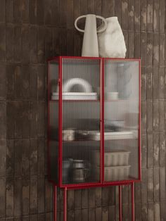 a red metal cabinet with glass doors on the top and bottom, in front of a brown tiled wall