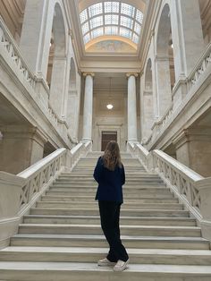 a woman standing at the bottom of stairs in a building with skylights above her