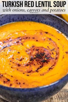 a blue bowl filled with carrot soup on top of a wooden table