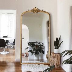 a large gold framed mirror sitting on top of a wooden floor next to a white chair