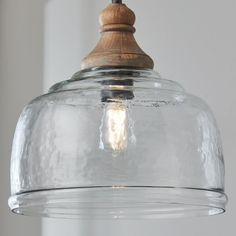 a clear glass light hanging from a ceiling fixture with a wooden top on the bottom