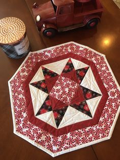 a quilted table topper with a red car in the background on a wooden table