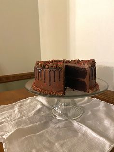 a chocolate cake sitting on top of a glass cake plate next to a white napkin