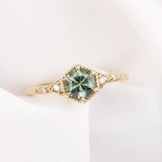 an engagement ring with a green and white diamond in the center on a white cloth