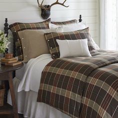 a bed with plaid comforter and pillows in a room next to a deer head