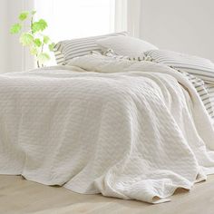 an unmade bed with white linens and striped pillow cases on the floor next to a potted plant