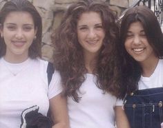 three young women standing next to each other in front of a stone wall and fence