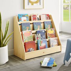 a children's book rack with books on it in a room next to a potted plant