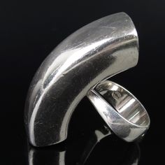 Astrid Fog (b. 1911-d. 1993) designed this 1970s Modernist sleek sculptural sterling ring for Georg Jensen, one of Denmark's most famous silversmith design companies. It has an large curvy elongated futuristic shape that is very shiny and reflective. The back has a curvy sturdy band mounted to it. The inside is signed "Georg Jensen" (incused lettering inside of a dotted oval - hallmark attributed to Georg Jensen beginning 1945). In my photo there was a little residue smudge over the hallmark, wh Sculptural Jewelry With Polished Finish For Formal Occasions, Contemporary Sculptural Jewelry For Formal Occasions, Modern Dome Ring For Anniversary, Contemporary Hallmarked Rings For Formal Occasions, Modern Open Bypass Ring For Formal Events, Modern Open Bypass Ring For Formal Occasions, Modern Bypass Open Ring For Formal Occasions, Modern Sterling Silver Dome Ring, Modern Silver Dome Ring