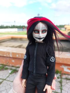 a hand holding a doll with makeup on it's face and long black hair