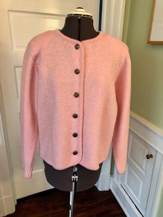 "A very traditional look. This cardigan sweater or knit suit jacket is made of 100% wool in a soft pink. It is unlined and has moderate shoulder pads. It features a crew neckline, long sleeves, and a front button closure with a ribbed binding on all edges that leaves a small scalloped edge. This garment is clean, with no stains, moth holes, or odors. Measurements to guide you: Bust: 42\" Waist: 42\" Sleeve: 26\" (quite long) Length from top of shoulder to hem: 24.5\" Decade: 80s Fabric: Wool Kni Elegant Pink Sweater With Button Closure, Elegant Pink Cardigan With Button Closure, Elegant Pink Knitted Sweater, Classic Fitted Pink Cardigan, Classic Pink Sweater For Spring, Fitted Classic Pink Cardigan, Classic Pink Spring Cardigan, Classic Pink Winter Outerwear, Pink Fitted Classic Sweater