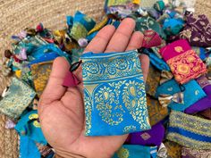 a hand holding a small blue and yellow cloth in front of a pile of colorful scarves