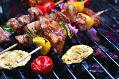 several skewers of meat and vegetables cooking on a grill