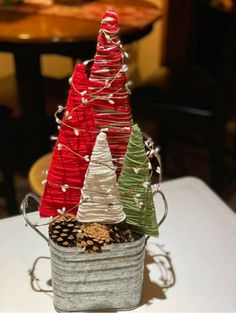 three small christmas trees sitting in a bucket on top of a table with pine cones