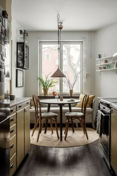 a dining room table and chairs in front of a large window with potted plants on it