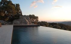 an empty swimming pool in front of a large rock formation at sunset or dawn with the sun setting on the horizon