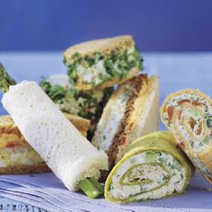 several different types of sandwiches on a blue cloth next to some breads and vegetables