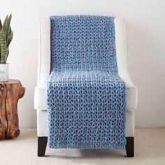 a blue crocheted blanket sitting on top of a white chair next to a potted plant