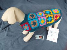 a stuffed dog wearing a colorful sweater next to a thank you card on a bed